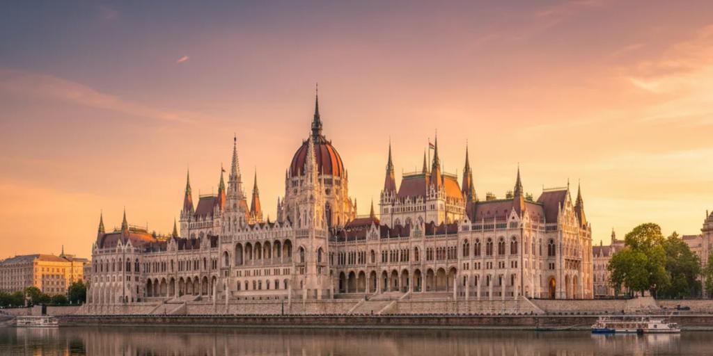 El Parlamento húngaro iluminado sobre el Danubio a la hora azul, visto desde el lado de Buda