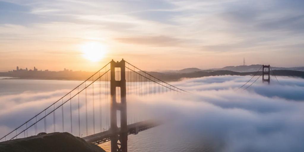 El Golden Gate Bridge emergiendo de la niebla baja al amanecer, las torres en International Orange contra un cielo pálido