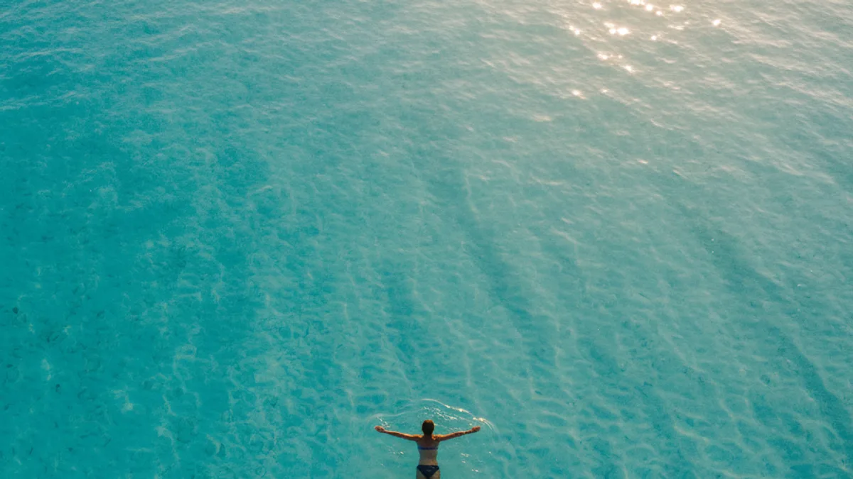 Bañista flotando de espaldas en aguas turquesas y transparentes, fotografiada desde arriba